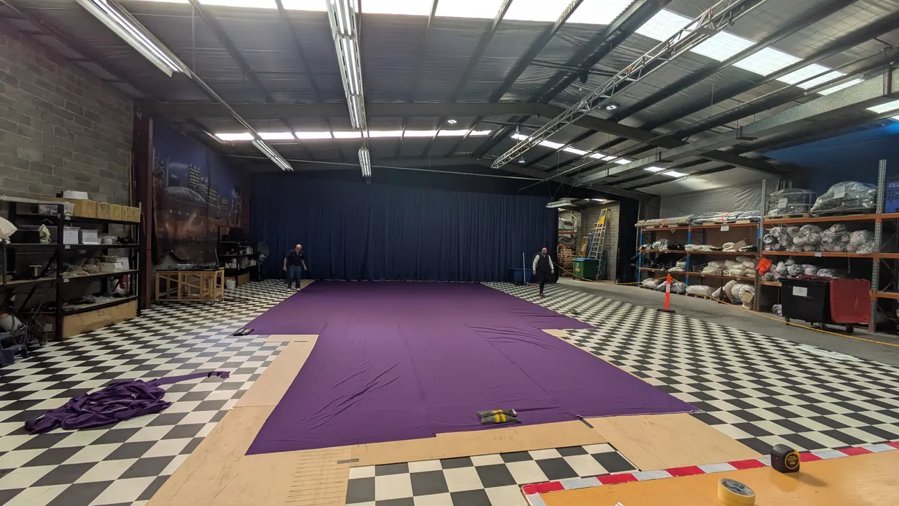A purple Come Alive roof swag laid out flat across the workshop floor, with two staff at the far end for scale